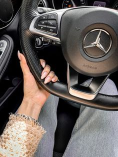 a woman is holding the steering wheel of a mercedes benz - benz car, with her hand on the steering wheel