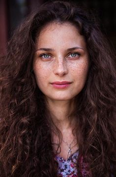 a woman with freckled hair and blue eyes looks into the camera while wearing a floral shirt