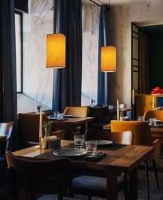 an empty restaurant with wooden tables and yellow chairs, blue drapes on the windows