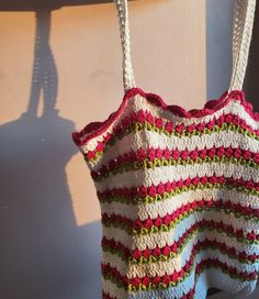 a crocheted bag hanging from a hook on a wall with the shadow of a person behind it