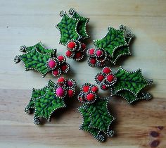 four christmas holly brooches sitting on top of a wooden table