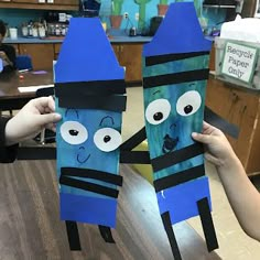 two people holding up paper bags with faces on them in the shape of crayons