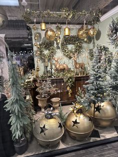 christmas trees and ornaments are on display in a store window with gold balls hanging from the ceiling