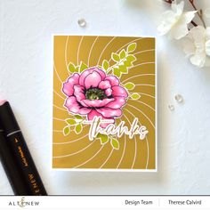 a close up of a flower on a card next to a pen and some flowers