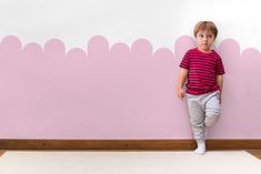 a little boy standing in front of a pink wall