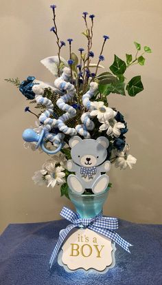 a blue vase filled with flowers and a teddy bear sitting on top of a table