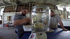 two men sitting at a table with a large glass jar filled with popcorn and another man standing next to it