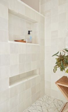 a white tiled bathroom with shelves and plants