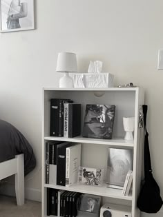 a white book shelf with books and pictures on the wall next to a bed in a bedroom