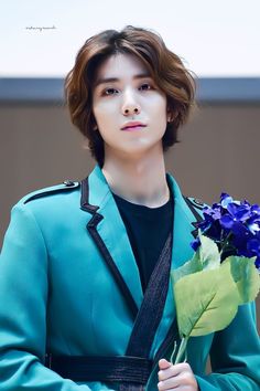 a young man in a blue coat holding a bouquet of flowers and looking off into the distance