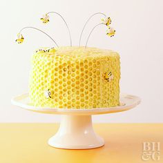 a yellow cake with honeycombs and bees on top sits on a white pedestal