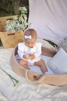 a baby sitting in a basket with pillows and flowers on the ground next to it