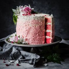 a pink cake with white frosting and flowers on top is sitting on a plate