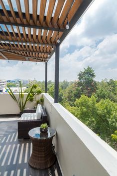 a balcony with chairs, tables and plants on the outside deck overlooking trees in the distance