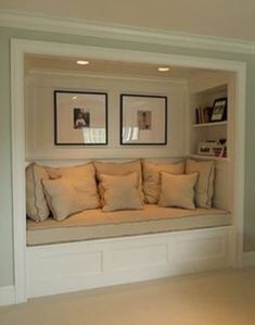 a window seat with pillows and pictures on the wall above it in a living room