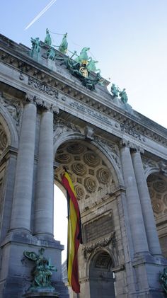 an arch with statues on top and a flag flying in the air over it's entrance