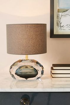 a glass table with a lamp and books on it next to a framed painting in the corner