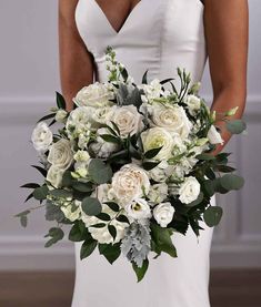 a bridal holding a bouquet of white flowers and greenery in her hands,