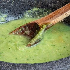 a wooden spoon in a black bowl filled with green liquid