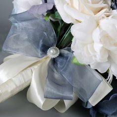 a bouquet of white flowers and blue ribbon with a pearl brooch on the center