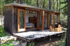 a small cabin in the woods with its doors open and furniture on the ground next to it