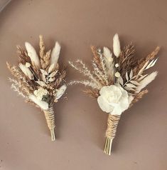 two boutonnieres with dried flowers and feathers on a brown plate, one is white