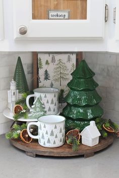 the kitchen counter is decorated for christmas with green trees and white mugs on it