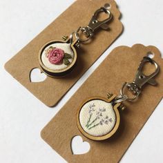 two keychains with flowers on them sitting next to each other in front of a tag