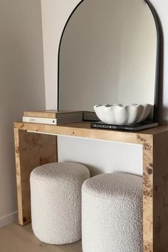 two white stools sitting under a mirror next to a table with a bowl on it