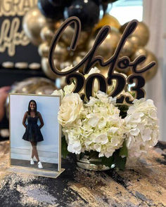 a table topped with flowers and a vase filled with white hydrangeas next to a cake topper