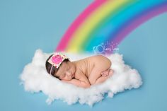 a baby sleeping on top of a cloud with a rainbow in the sky behind it