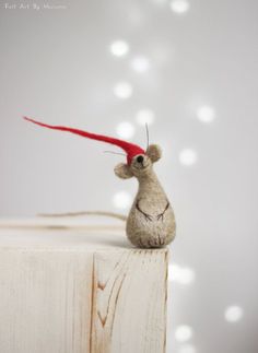 a small mouse with a red hat on top of it's head sitting on a piece of wood