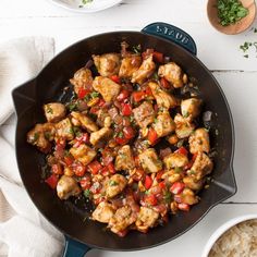 a skillet filled with chicken and vegetables on top of a white table next to rice