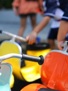 two people standing next to colorful scooters on the street and one person is holding something in his hand