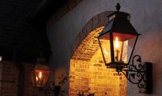 an old fashioned light hanging from the side of a brick building with two lit candles on it