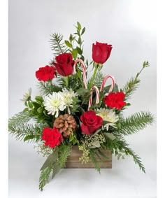 a christmas arrangement with candy canes, roses and greenery in a wooden box