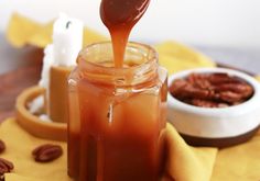 caramel sauce being drizzled into a jar with pecans in the background