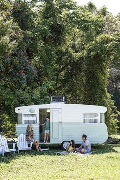 people sitting on lawn chairs in front of an old camper with the door open