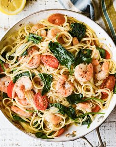 pasta with shrimp, spinach and tomatoes in a skillet on a white table