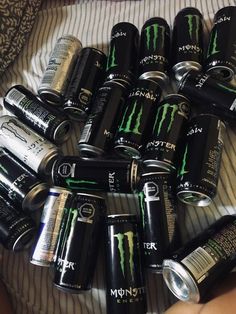 a pile of monster energy drinks sitting on top of a bed