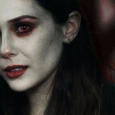 a woman with blood on her face and dark hair is staring at the camera while she has red eyes