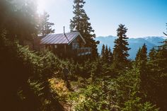 a man walking up a trail in the woods towards a cabin on top of a mountain