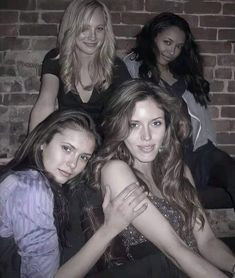 three women are sitting next to each other in front of a brick wall with their arms around one another