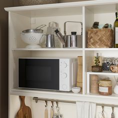 a microwave oven sitting on top of a white shelf filled with utensils and other kitchen items