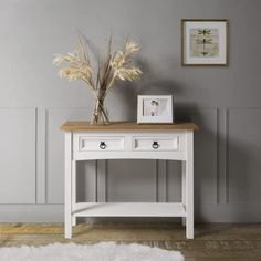 a white wooden table with two drawers and a vase on top of it next to a wall