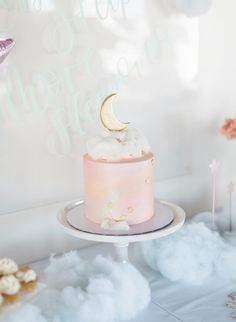 there is a pink cake with a moon on top and clouds in the back ground