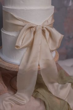 a three tiered white cake with a bow on it's top and ribbon around the base