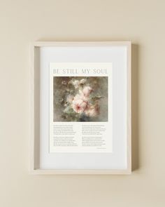 a white framed print with the words be still my soul and flowers in it on a beige wall