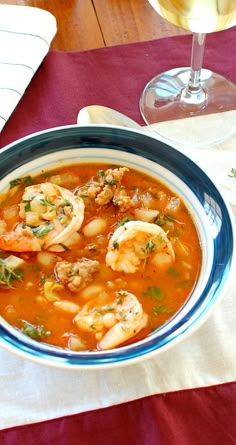 a bowl of shrimp and tomato soup on a table next to a glass of wine