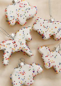 four decorated cookies with sprinkles are arranged on a white tablecloth and one has a silver ornament in the shape of a polar bear